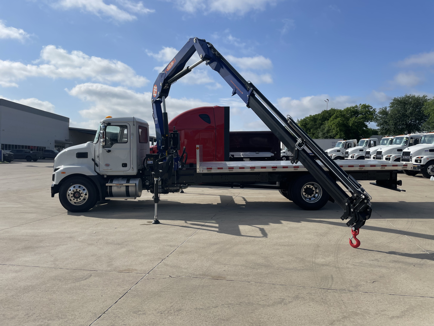 Mack MD7 boom truck side view showing folding articulating crane with hook, white cab, red body, black boom, parked on lot