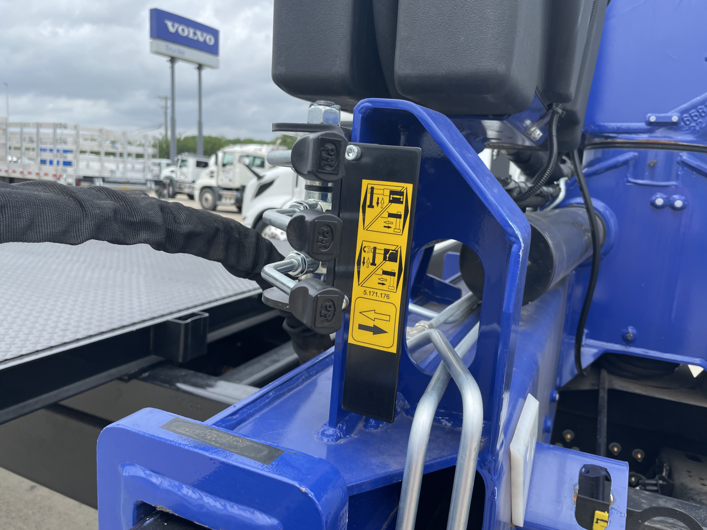 Boom truck chassis with hydraulic hose connections and warning labels on a blue MACK MD7 cab, showing hydraulic control block and sticker labels.