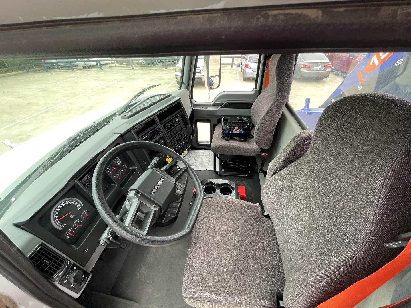 Cab interior of a 2025 Mack MD7 truck showing steering wheel, dashboard gauges, driver seat, and center console with cup holders.