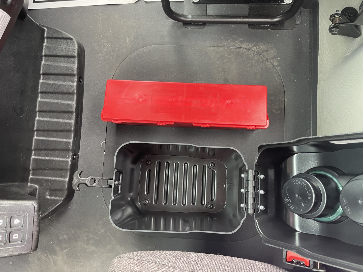 In-cab storage area of a Mack MD7 truck showing a red rectangular item and a small open compartment with a ribbed bottom panel, plus part of a cup holder and control panel.
