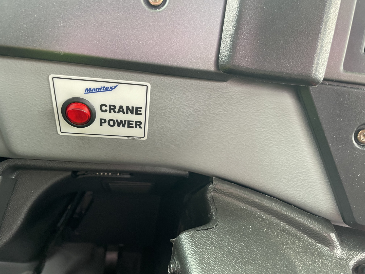 Manitou crane power sticker on a Mack MD7 dashboard area with a red push button and textured gray plastic