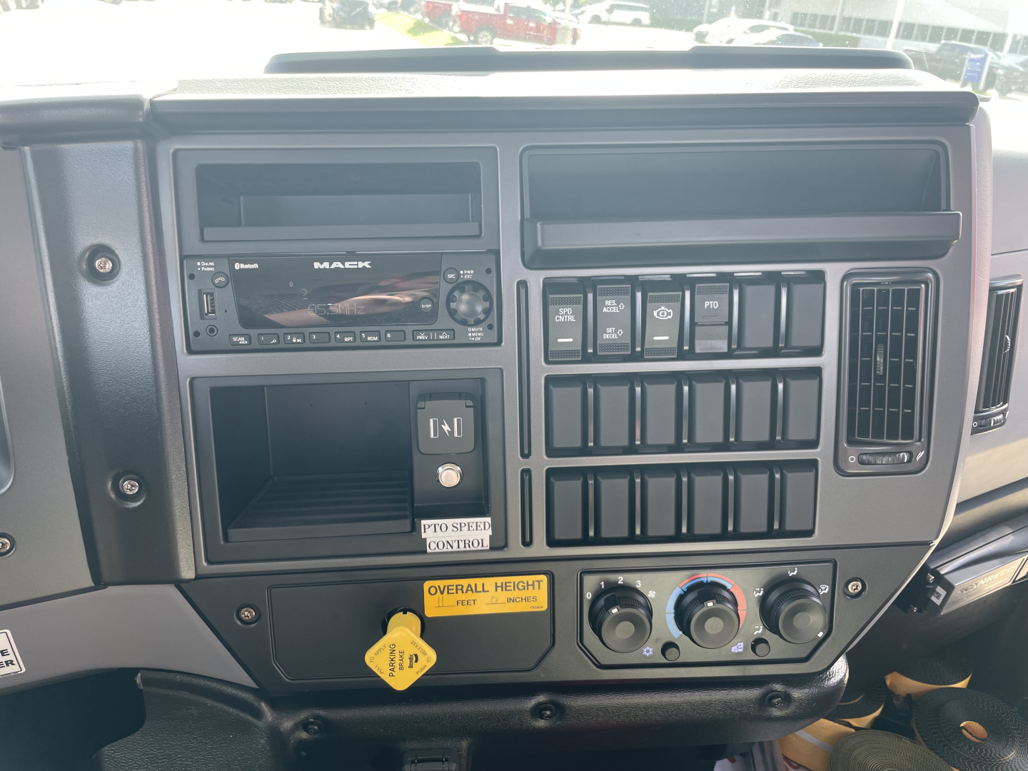 Mack MD7 dashboard showing radio unit, multiple switch panels, climate controls, and a yellow “Overall Height” placard. dashboard text includes 'MACK' on radio and various blank slots.