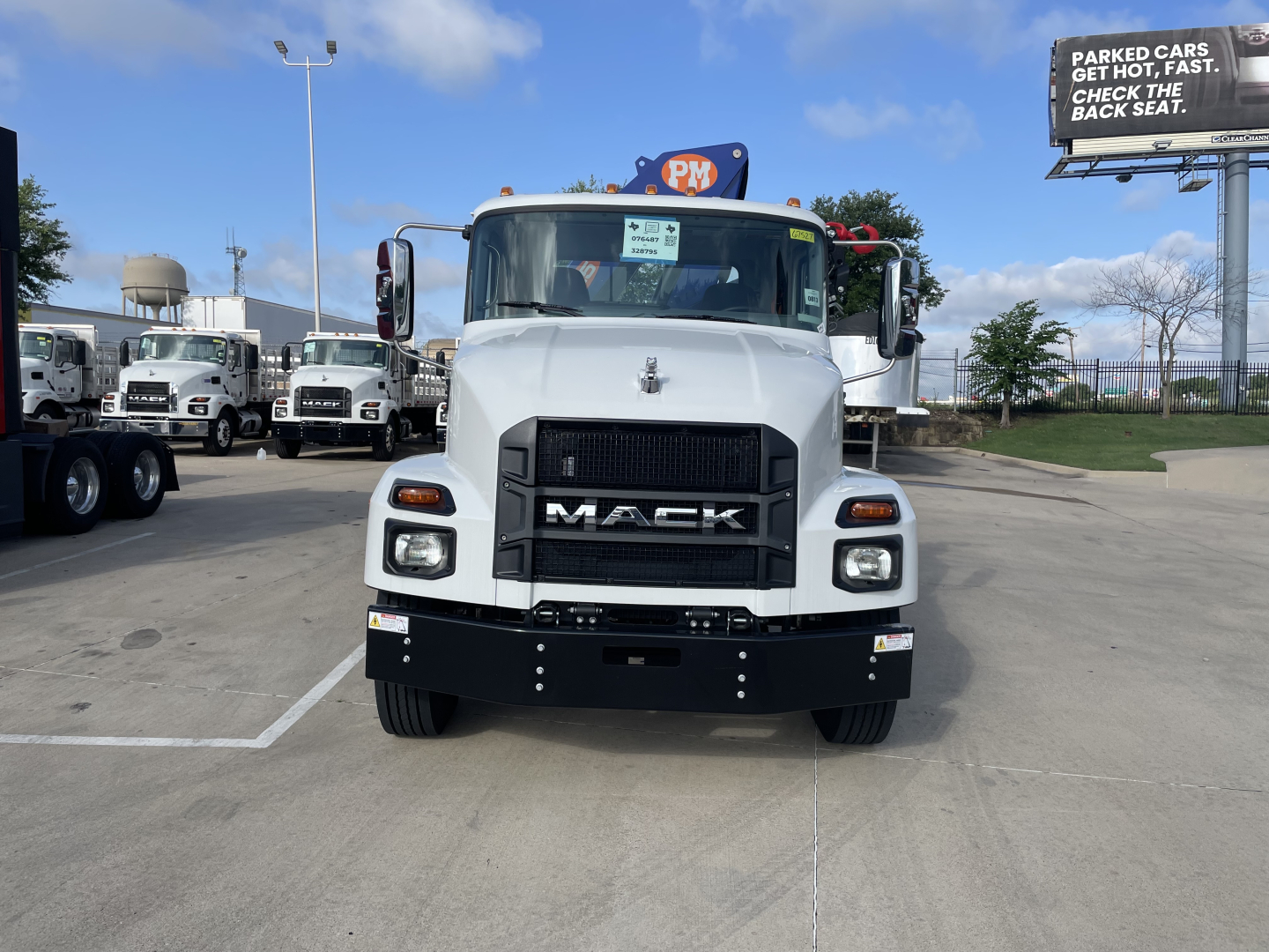 Front view of a white 2025 Mack MD7 truck in a dealership lot showing the grille with MACK lettering and headlights.