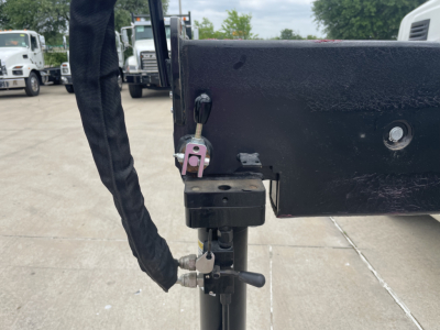 Truck hitch area showing a locking pin and hydraulic cylinder on a black frame with a pink padlock and braided protective sleeve.