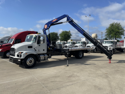 New Mack MD7 truck with blue knuckle boom arm extended, white cab, in a dealership lot with other trucks