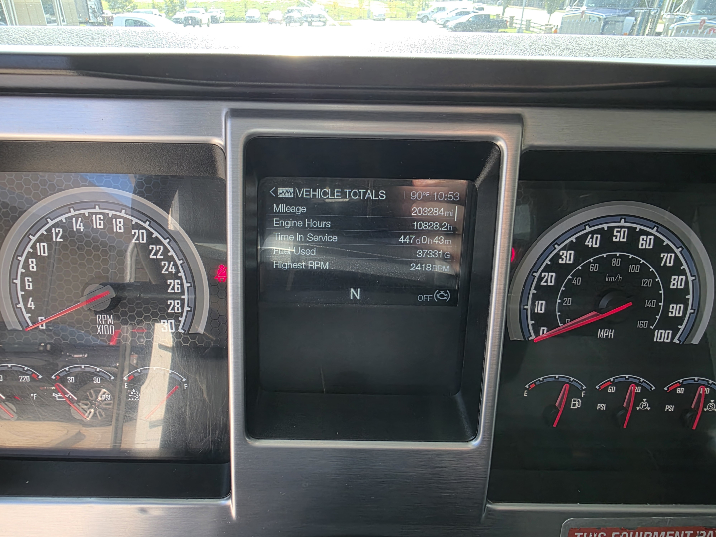 Mack Granite truck dashboard close-up showing instrument clusters and a central digital display with vehicle totals including mileage, engine hours, and uptime.
