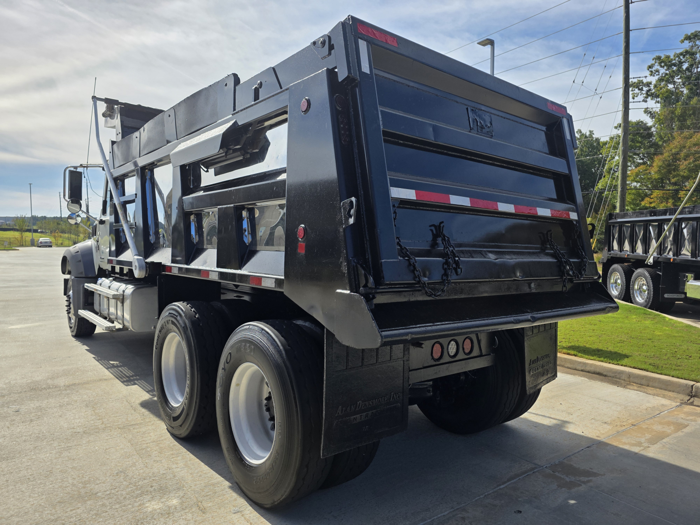 Dump truck rear view showing Mack GRANITE dump bed with black painted body, dual rear axles, mud flaps, and reflective striping.