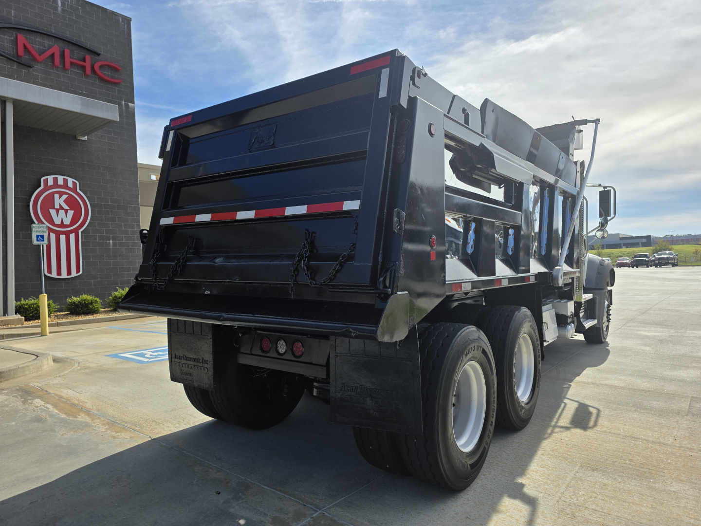 Dump truck rear and side view of a 2022 Mack Granite dump truck, black with reflective red/white stripes, dual rear axles, hydraulic dump bed, visible tires and wheel wells.