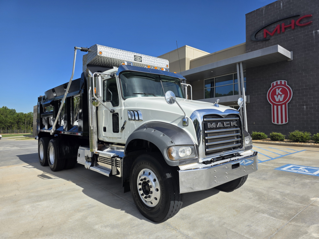 Dump truck showing 2022 Mack Granite with chrome grille and dual rear axles; cab side mirrors; large front bumper; KW dealership building in background.