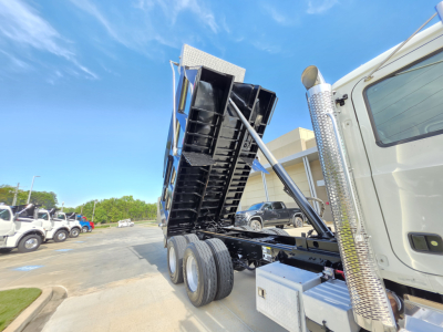 Dump truck bed raised on a 2022 Mack Granite showing tilt hydraulics, dual rear axles, chrome exhaust stacks, and service toolbox on the side.