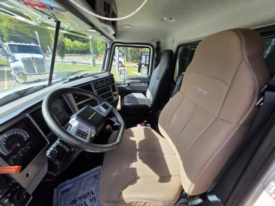 Interior of a 2022 Mack GRANITE dump truck cab showing steering wheel, dashboard gauges, beige fabric driver seat, and side door window.