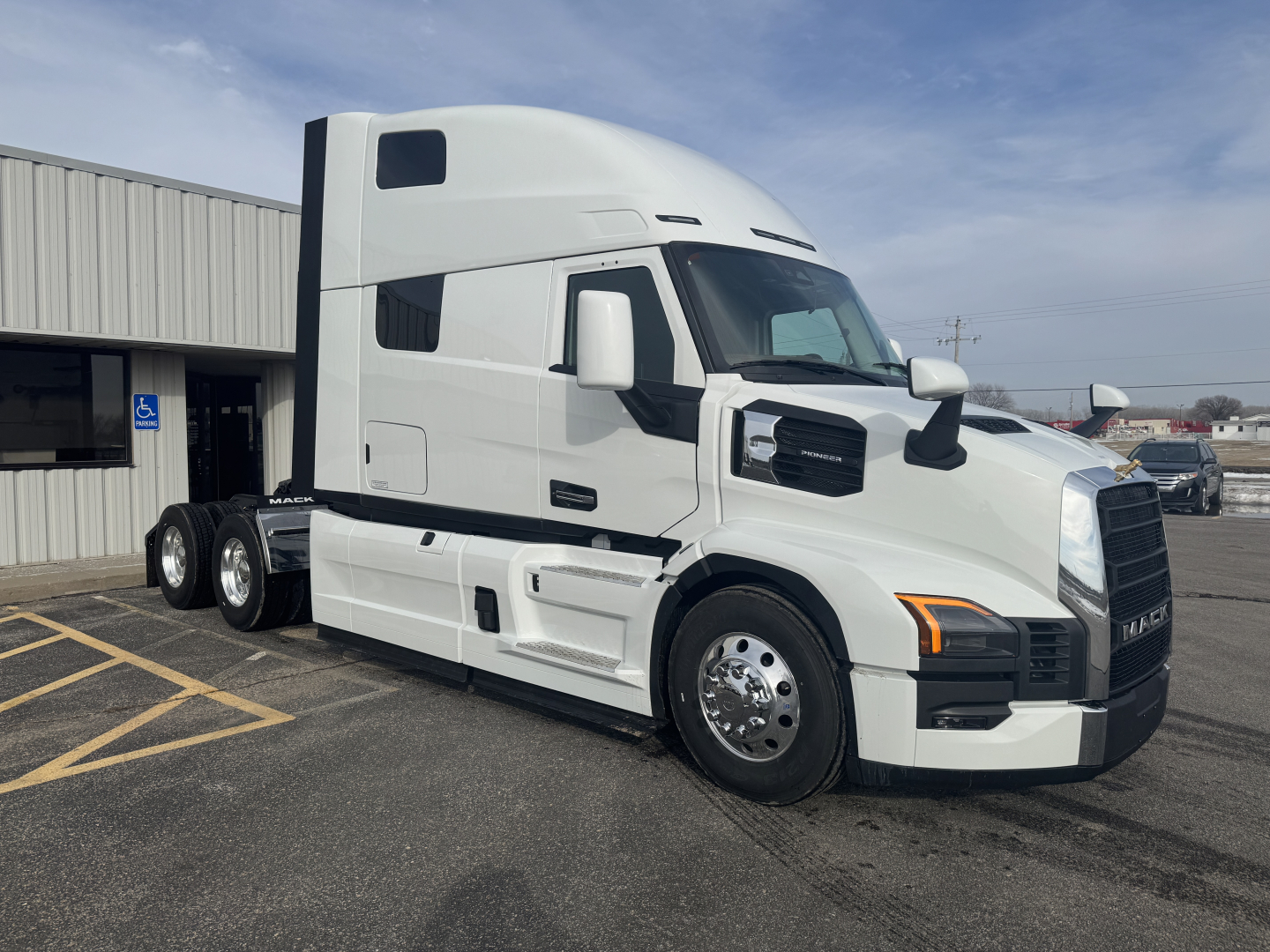 Truck cab of a white 2026 Mack PR64T76H conventional sleeper tractor, front right side view, with black grille and large mirrors.