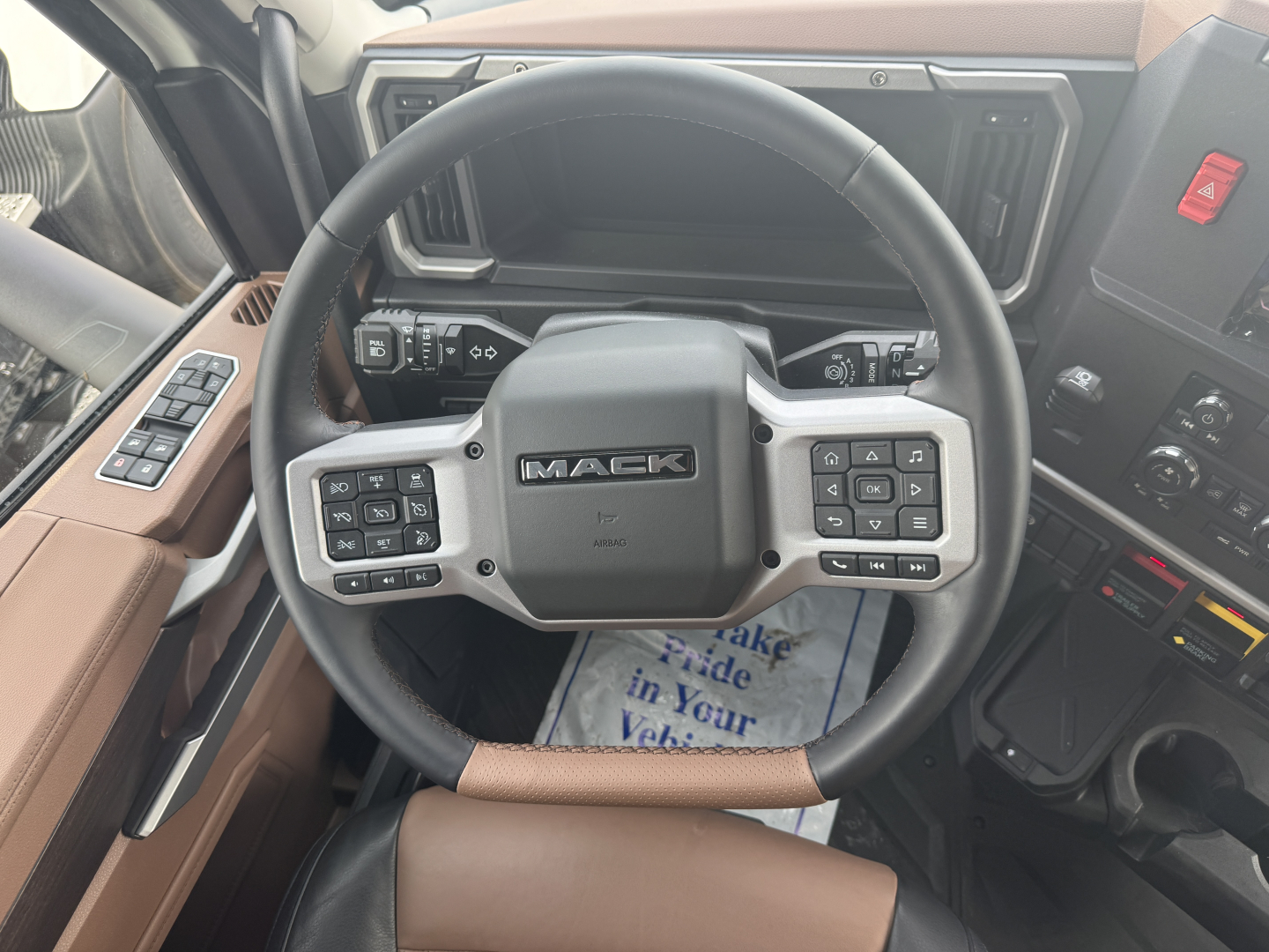 Interior view of a Mack truck steering wheel with multiple control buttons and dashboard panels visible.