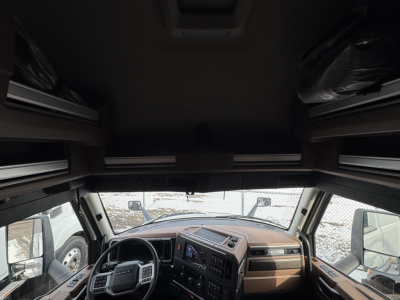 Cab interior of a new 2026 Mack PR64T76H sleeper cab showing dash, steering wheel, infotainment screen, and overhead bunks.