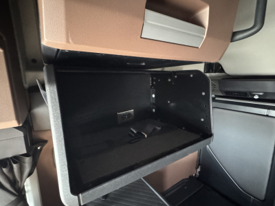 Truck interior front cabin area showing open glove box and surrounding panels in brown and black; visible screws and interior trim.