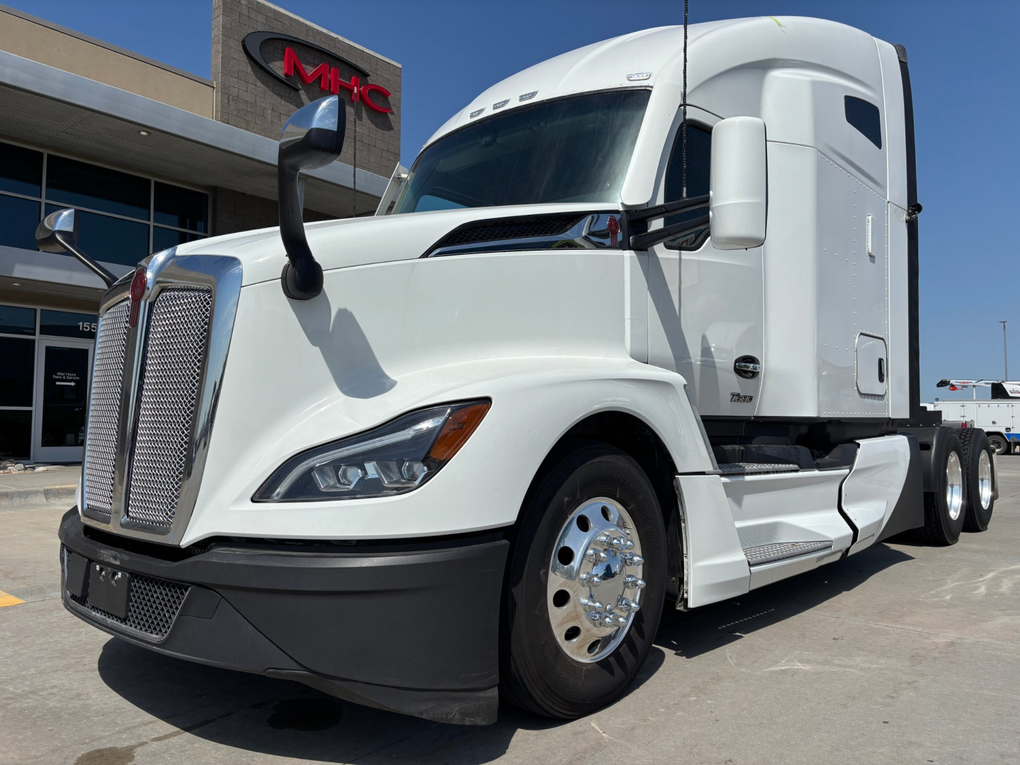 Kenworth T680 2022 white sleeper cab truck side front view showing grille, headlight, and large side mirrors.