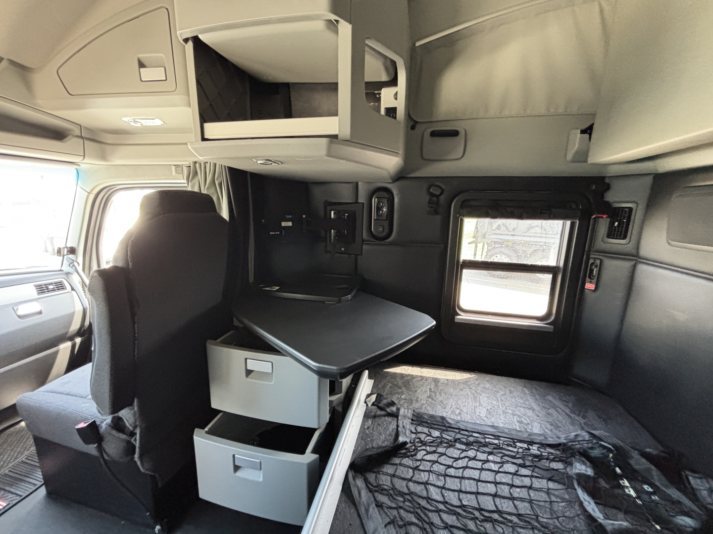 Kenworth T680 truck cab interior showing sleeper area with overhead cabinet, side window, and open storage drawers.