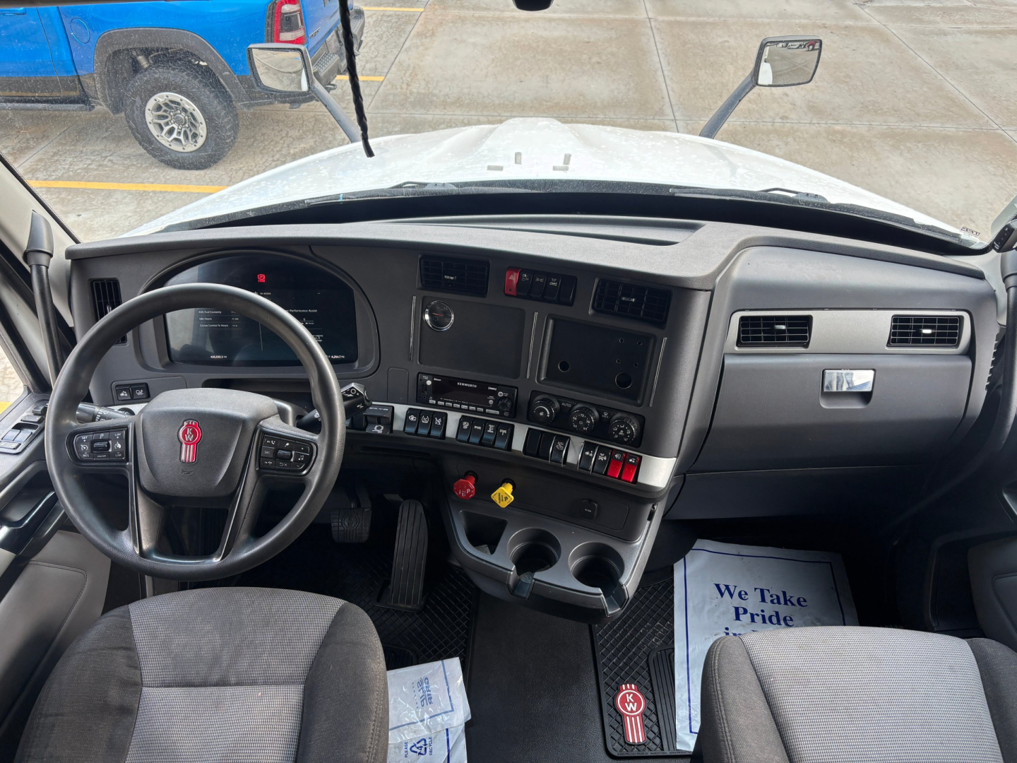 Kenworth T680 cabin dashboard view showing steering wheel, instrument cluster, center console with switches, and dual cup holders.