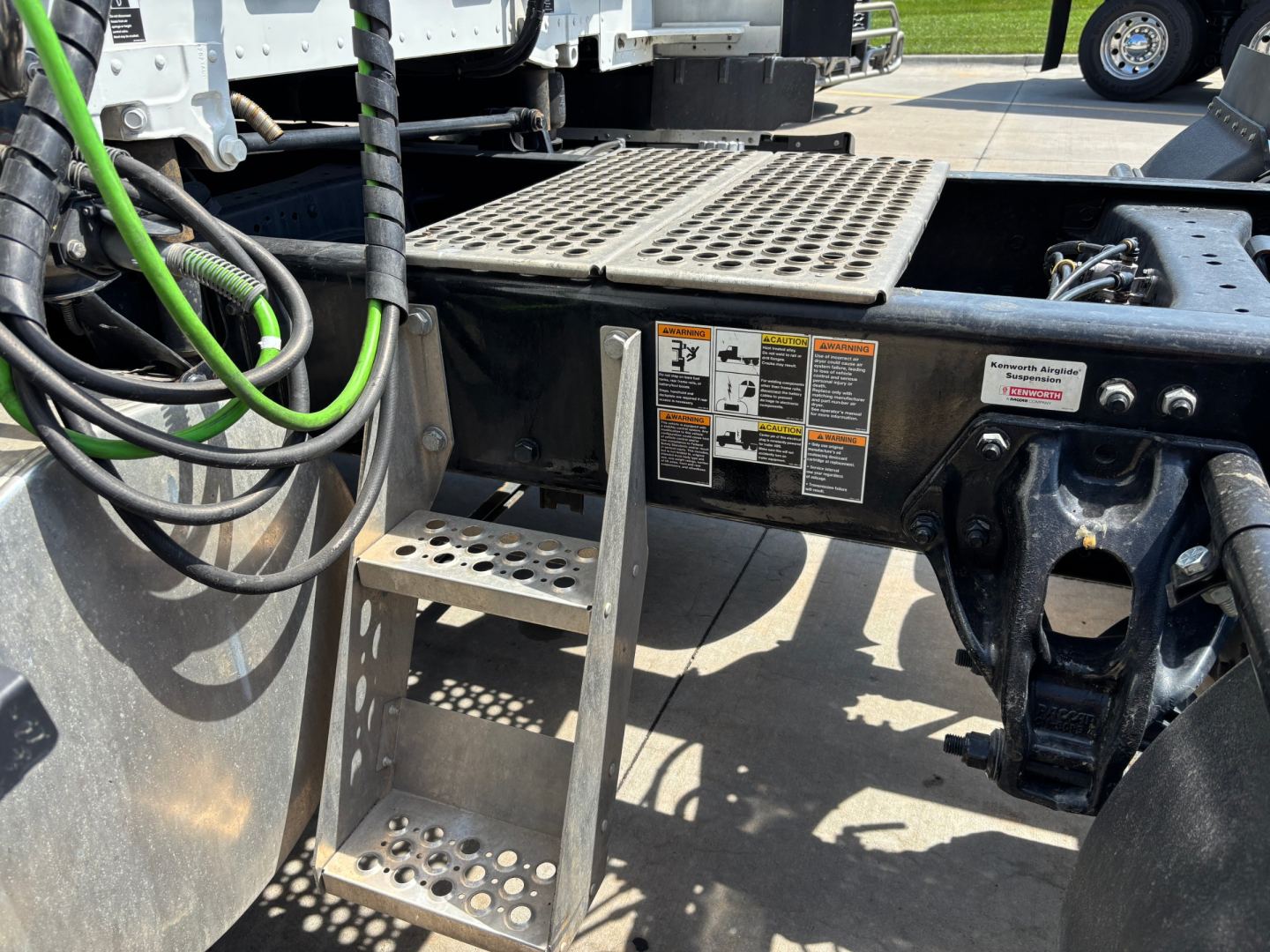 Kenworth truck chassis step and platform with warning labels and cables visible in the chassis area.