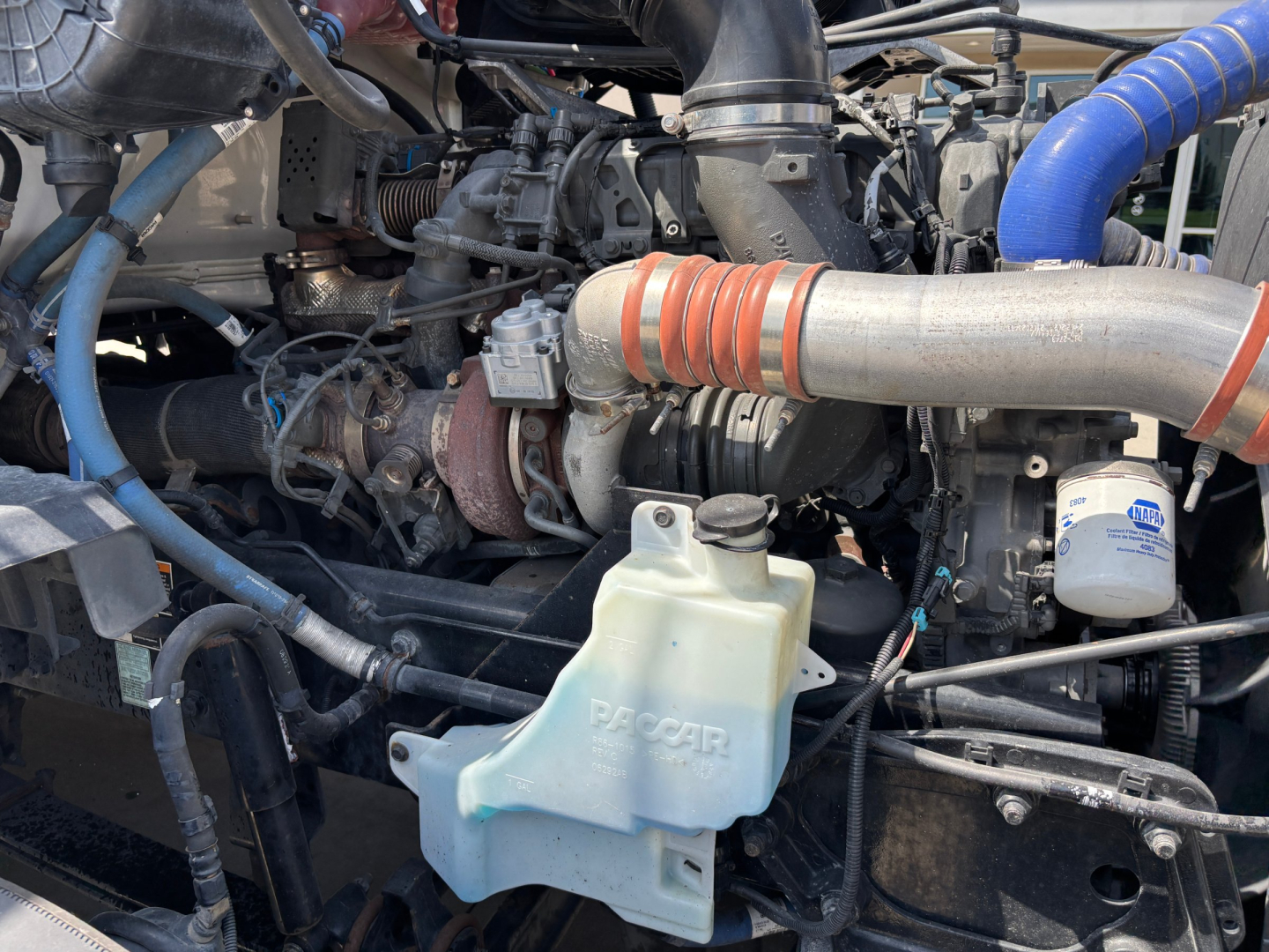 Kenworth T680 engine bay showing coolant reservoir and turbo hose with blue silicone hose.