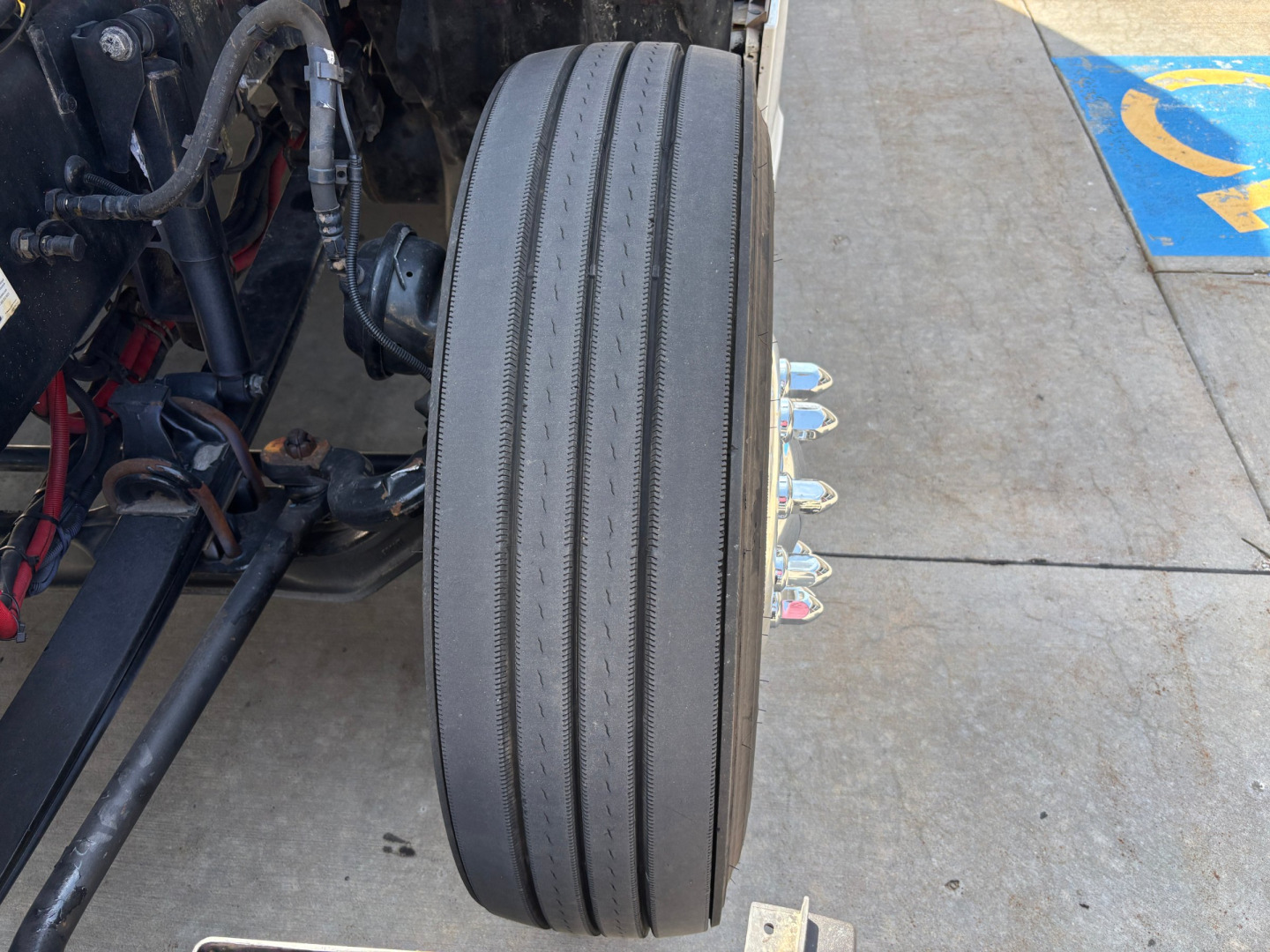 Kenworth T680 front wheel and suspension components visible with air lines and brake drums.