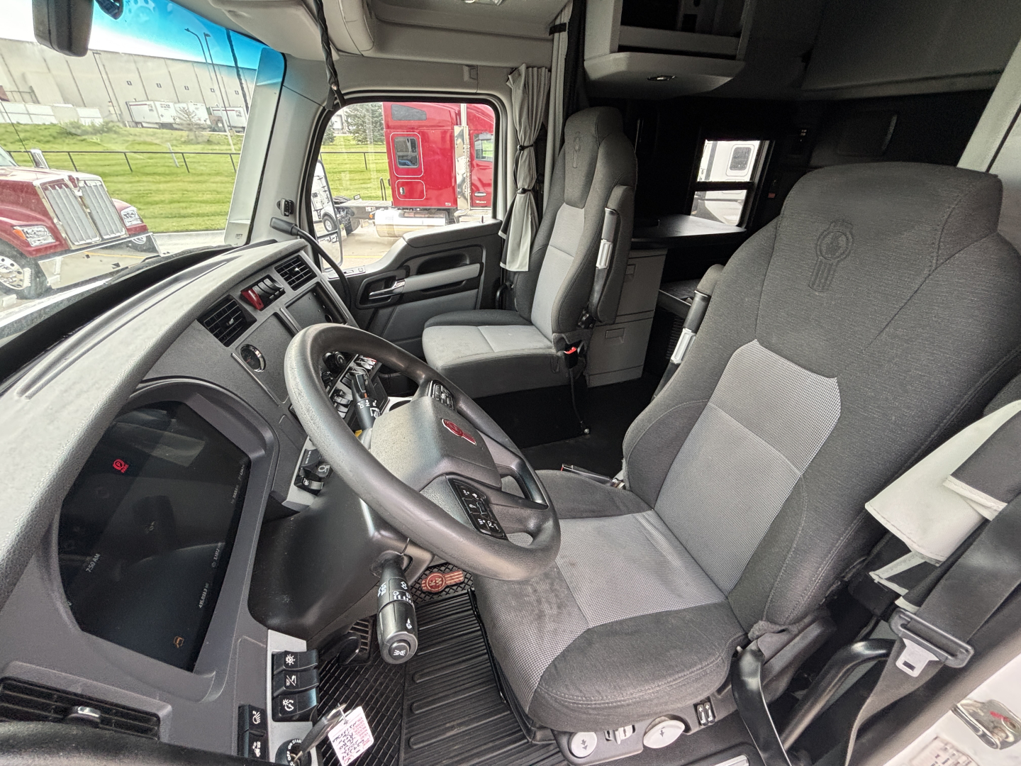 Truck cab interior showing steering wheel and driver's seat of a Kenworth T680, with dashboard and passenger seat visible.