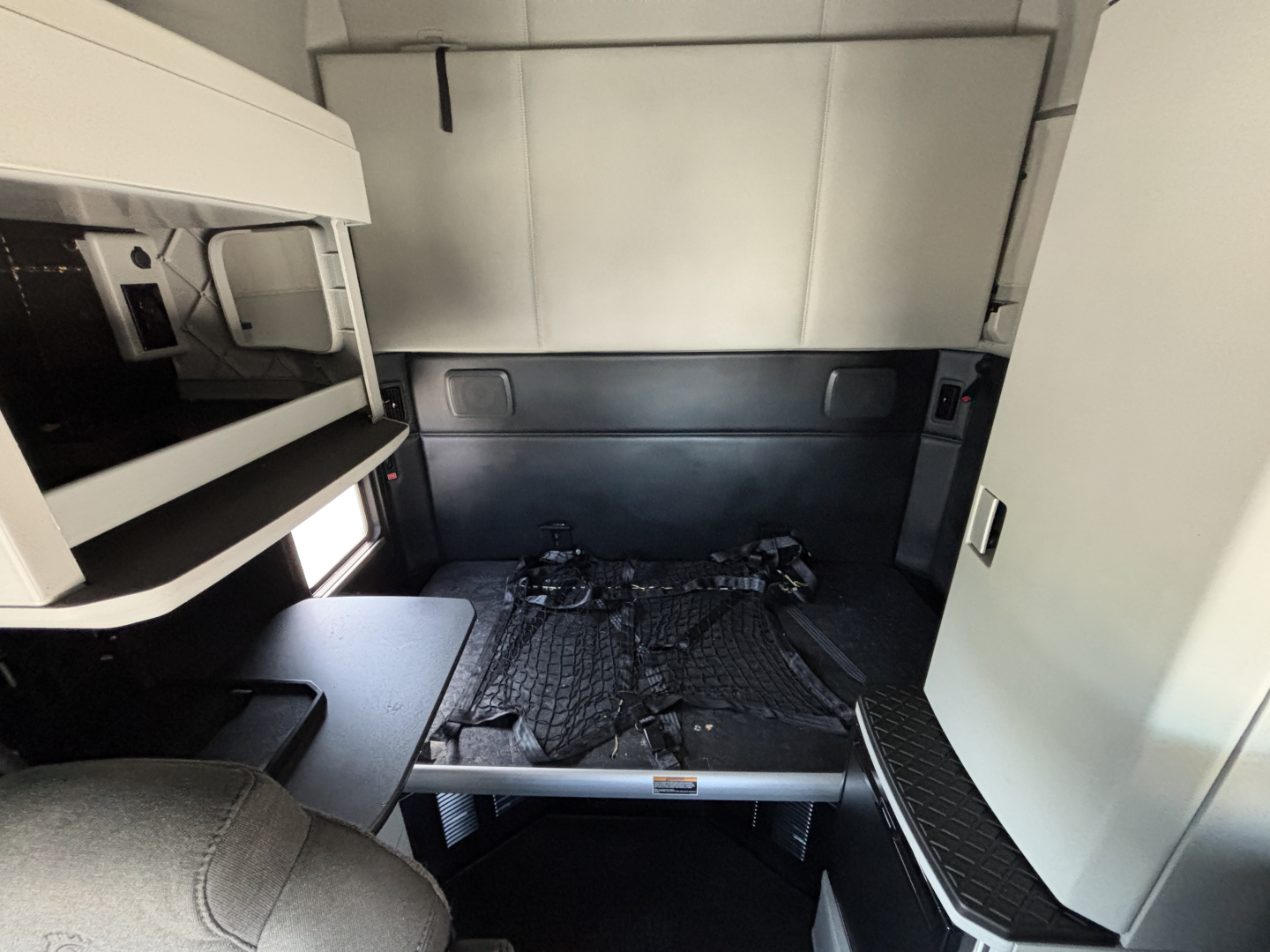 Kenworth T680 sleeper cab interior showing cargo area with bed frame and tie-downs, side wall panels, and overhead storage shelf.