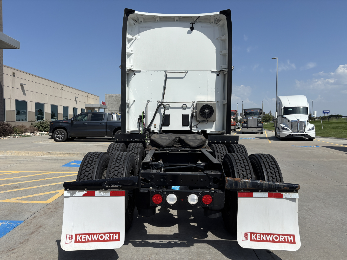 Kenworth heavy-duty truck chassis rear view showing fifth wheel, dual rear axles, and Kenworth mud flaps in a parking lot.