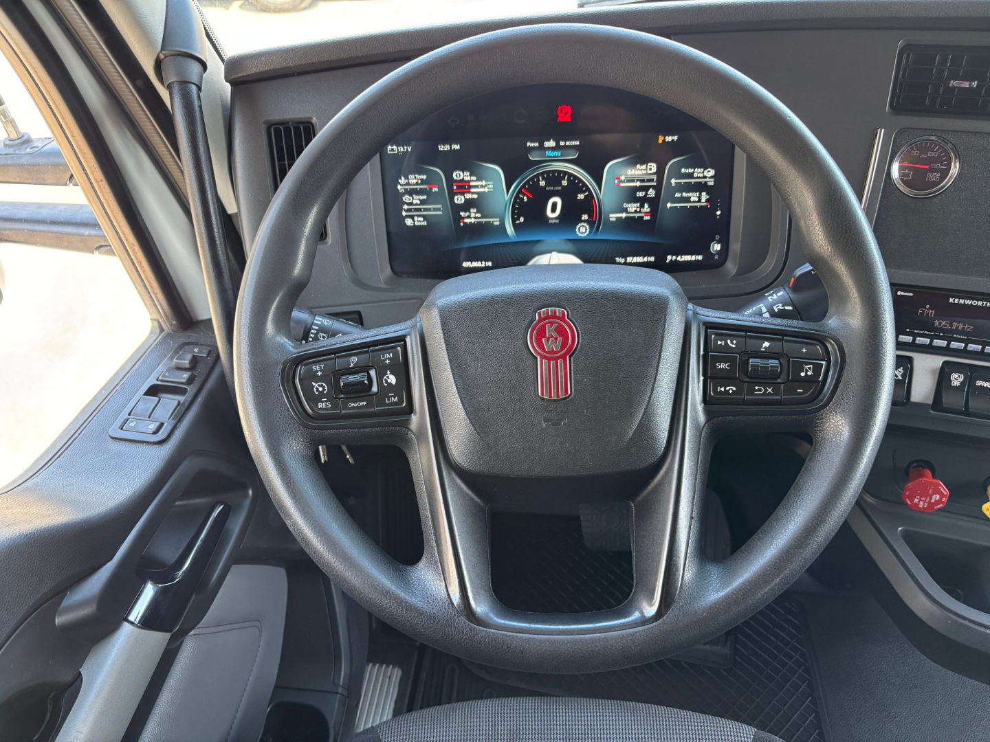 Kenworth T680 steering wheel and dashboard showing digital gauges; steering wheel with Kenworth badge, multiple control buttons, and digital instrument cluster.