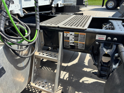 Kenworth truck chassis step and platform with warning labels and cables visible in the chassis area.