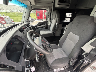 Truck cab interior showing steering wheel and driver's seat of a Kenworth T680, with dashboard and passenger seat visible.