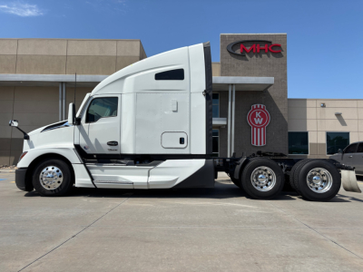 Kenworth T680 tractor in front of dealer building, side view showing cab and chassis with dual rear axles.