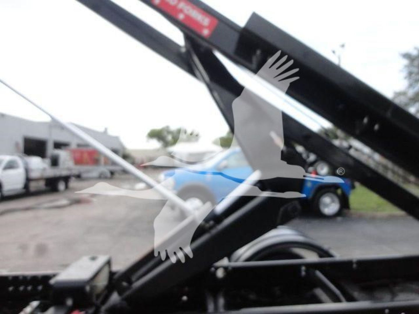 Truck hoist mechanism on a 2023 Chevrolet Silverado 5500HD with hydraulic arm and black metal frame. Faint background shows other vehicles.