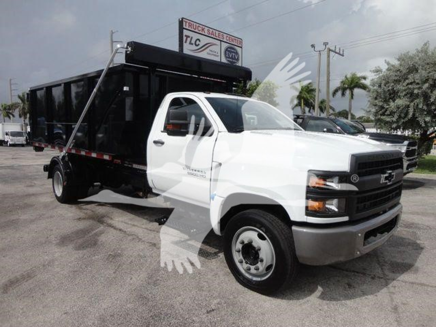 Chevrolet Silverado 5500HD roll-off truck with white cab and black dump body, side view.