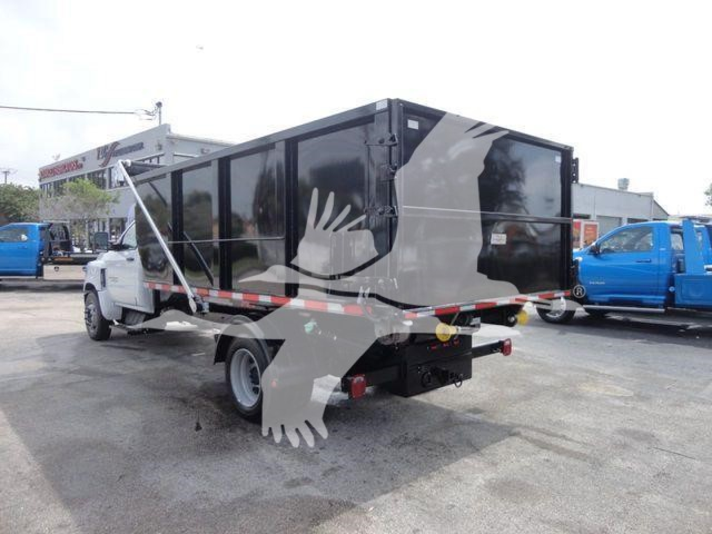 Chevrolet Silverado 5500HD roll-off truck with black-and-gray dump body, side-view, rear hitch, in a dealership lot.