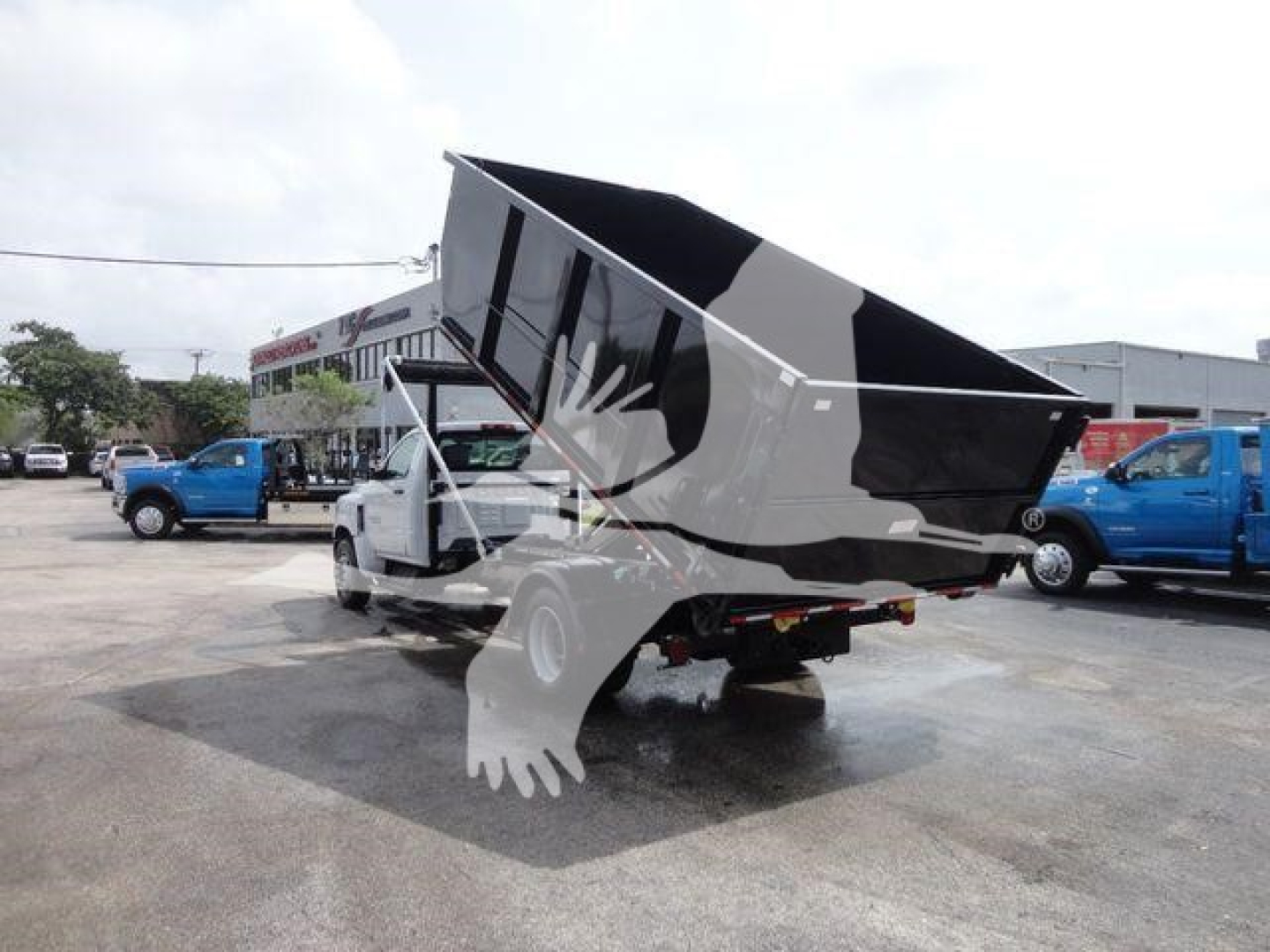 Chevrolet Silverado 5500HD roll-off truck with dump bed raised, visible on a dealership lot. No legible labels or serial numbers clear in this view.