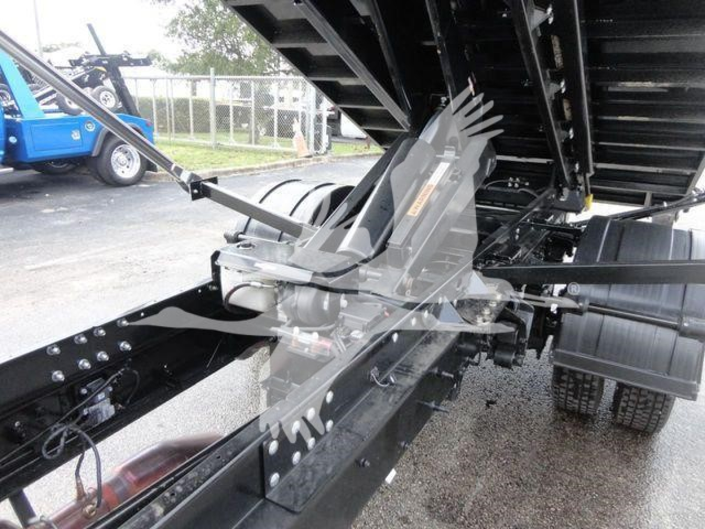 Truck chassis and hoisting mechanism of a 2023 Chevrolet Silverado 5500HD roll-off truck showing hydraulic cylinders and underbody components.