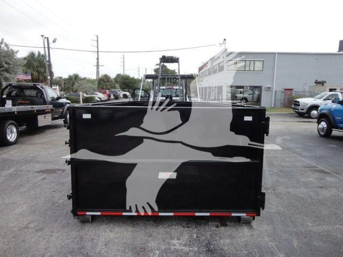 Back of a black dump trailer with a white graphic of a bird in flight on the tailgate; red-and-white reflective strip along the bottom edge; no visible text readable.