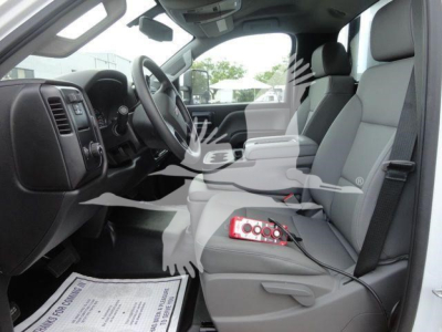Interior of a 2023 Chevrolet Silverado 5500HD cab showing front seats and dashboard with a red electrical jumper and cables on the passenger seat.