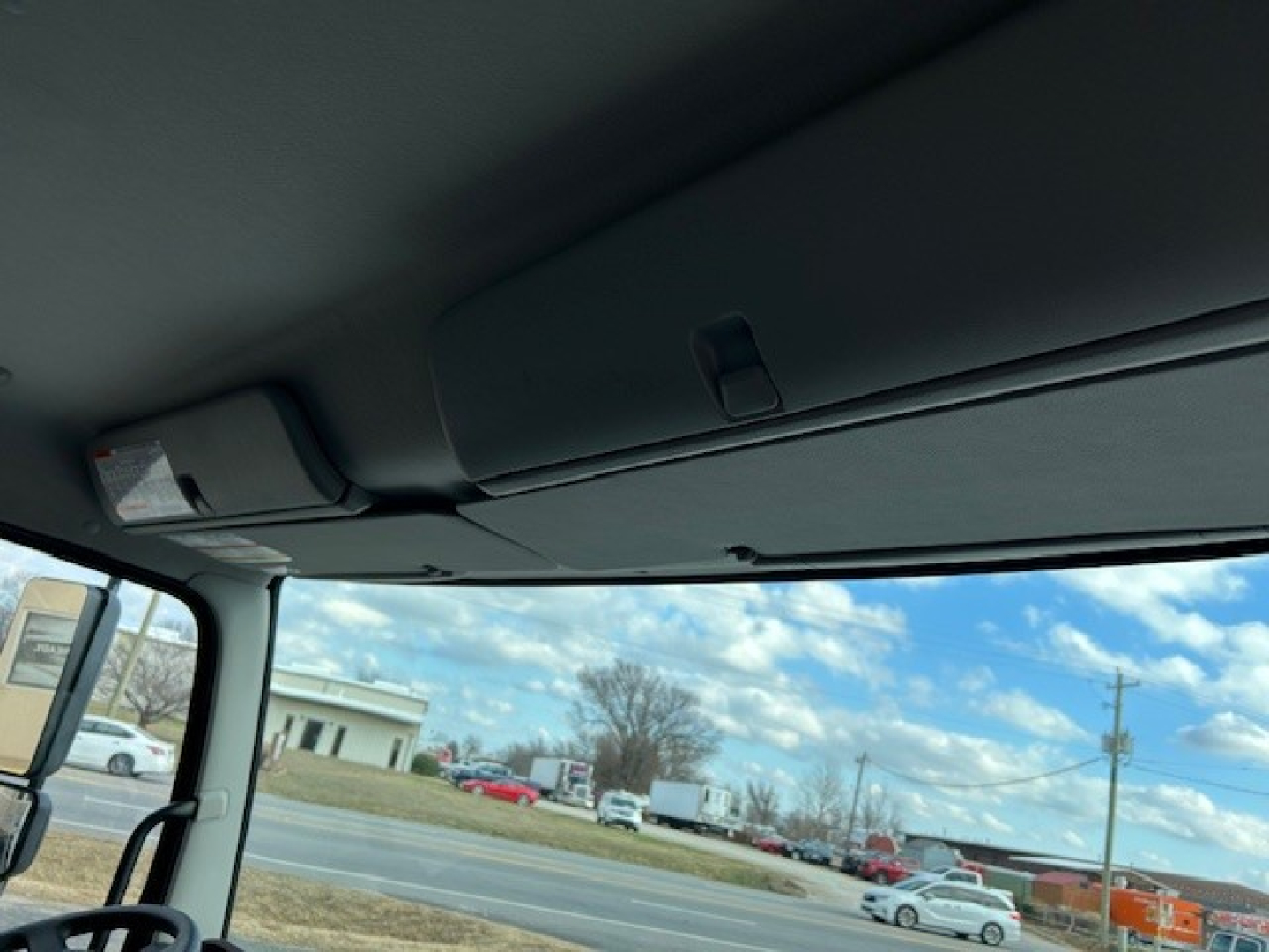 Cab and chassis truck interior view showing sun visor and windshield from driver seat with blue sky and parking lot outside.
