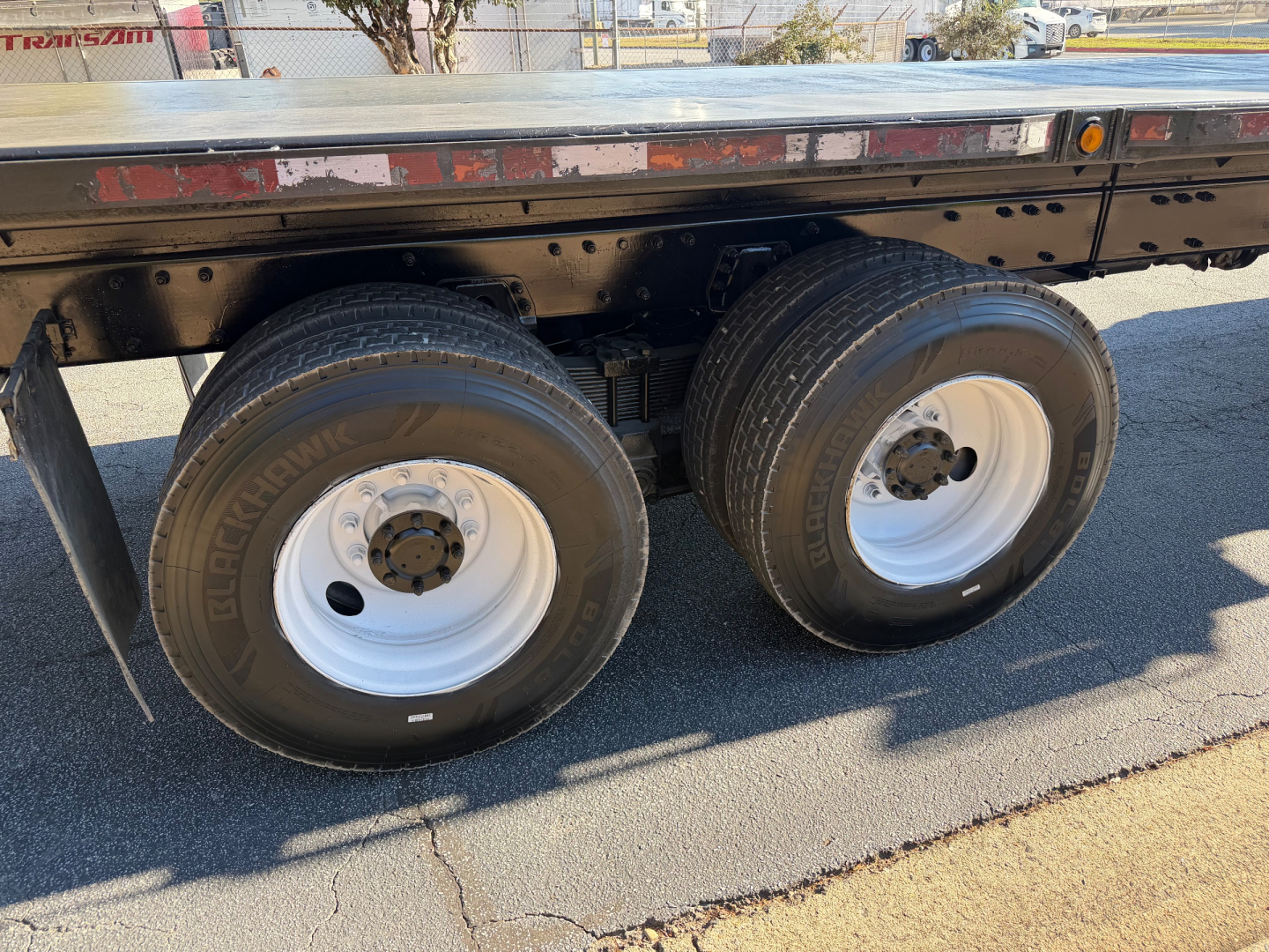 Flatbed truck rear dual axle wheels with white rims and black tires, side frame of trailer visible under metal deck.