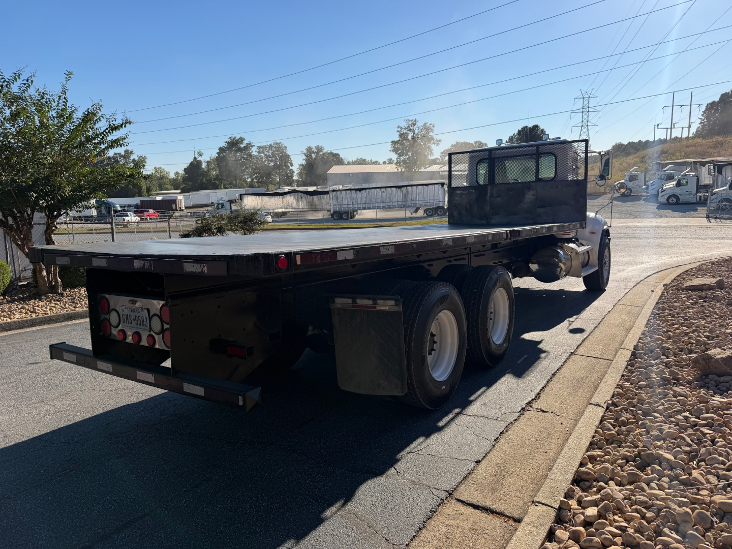 Truck rear and flatbed of a 2007 Peterbilt 335 flatbed truck showing dual rear axles and a black cab with sleeper design. The flatbed has a metal deck with taillights and a bumper; no visible text readable on the body.