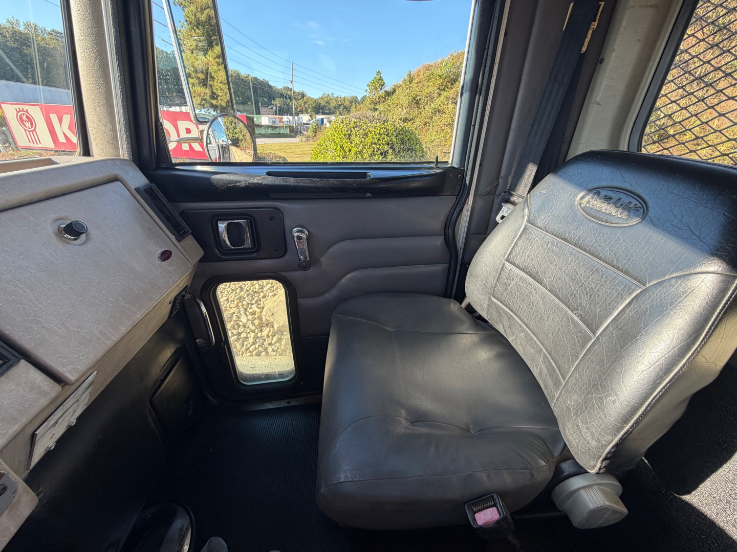 Peterbilt truck cab interior showing driver-side door panel, window, and bench seat with black vinyl upholstery.