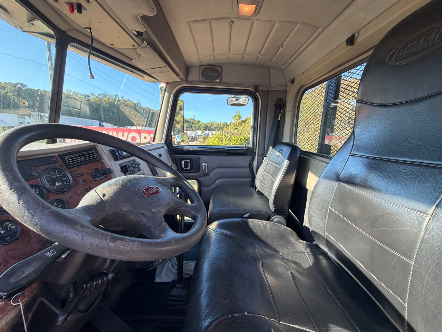 Peterbilt truck cabin interior with steering wheel, dashboard, and seating; view through driver door window showing seat and overhead console.