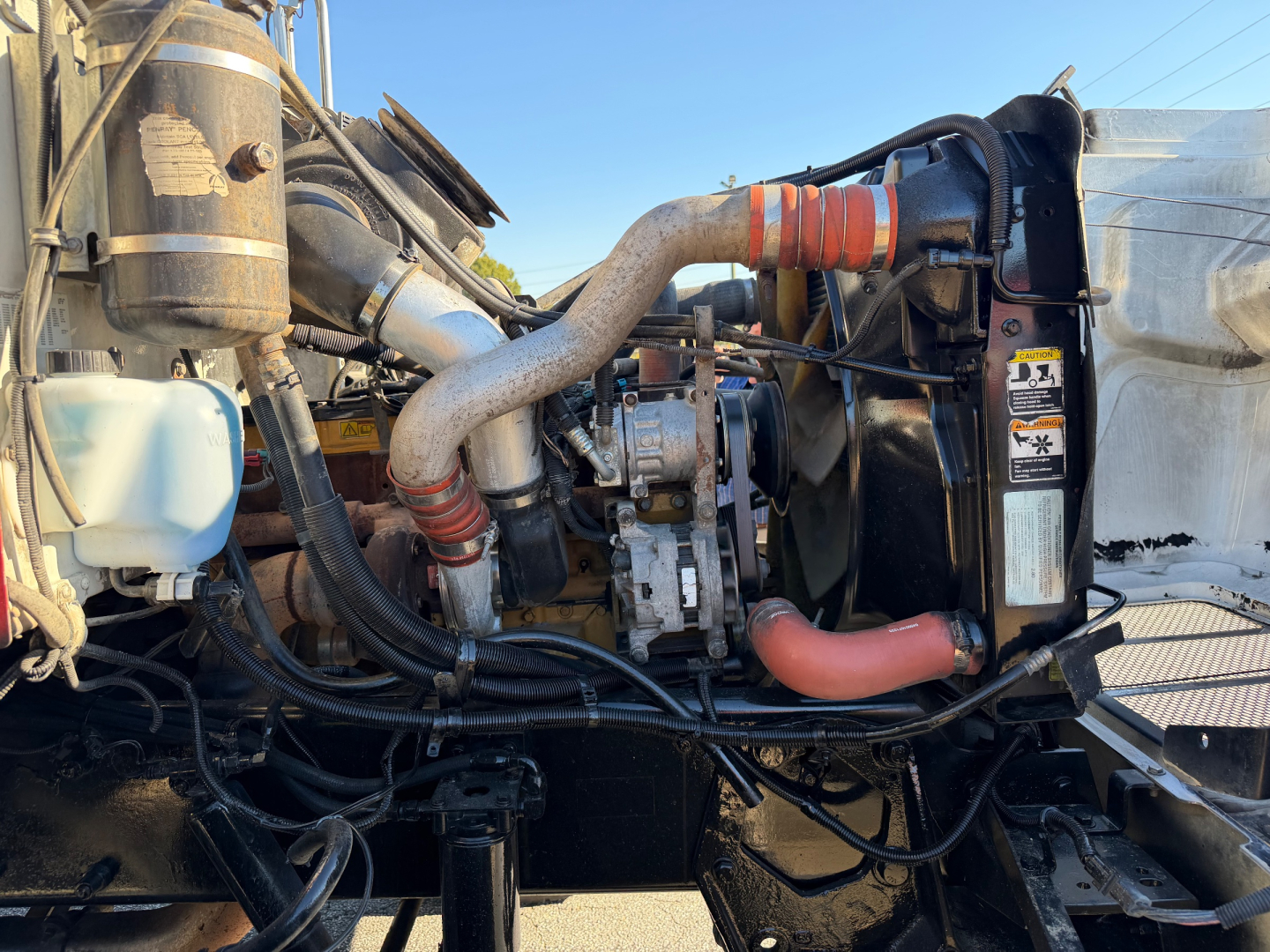 Peterbilt 335 engine bay showing turbocharger, hoses, and radiator with pink coolant hose and various labels.