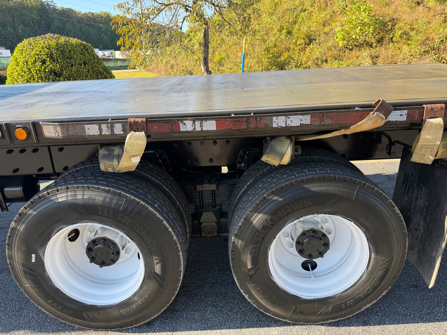 Peterbilt flatbed truck side view showing dual rear wheels and flatbed deck with tiedown straps and undercarriage components.