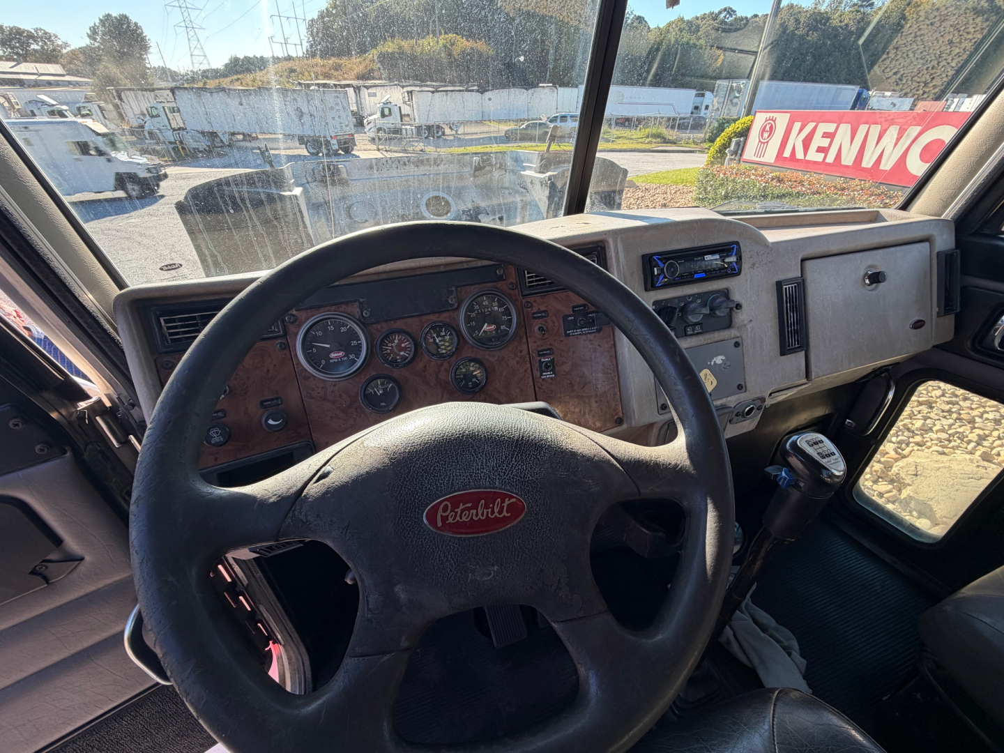 Peterbilt 335 truck interior steering wheel and dashboard with woodgrain panel, gauges, and Kenwood head unit visible.