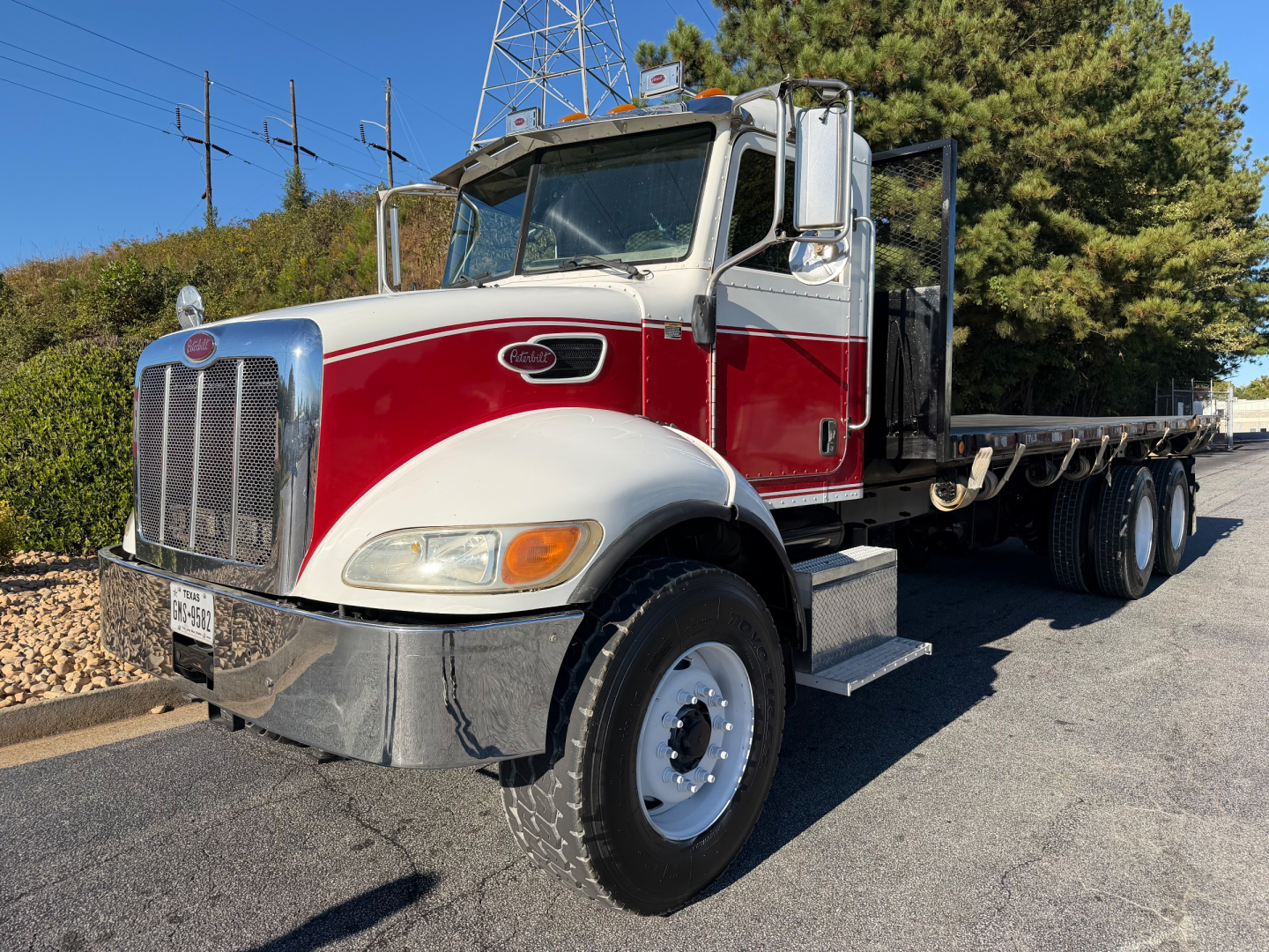 Peterbilt 335 truck with red and white cab, flatbed, large chrome grille, dual mirrors, daytime running lights, parked on asphalt.