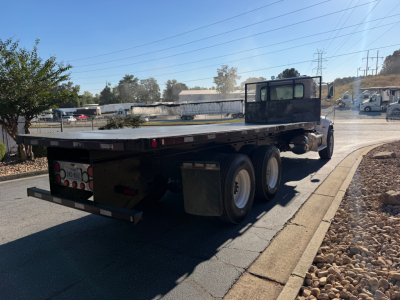 Truck rear and flatbed of a 2007 Peterbilt 335 flatbed truck showing dual rear axles and a black cab with sleeper design. The flatbed has a metal deck with taillights and a bumper; no visible text readable on the body.