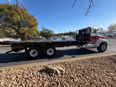 Peterbilt 335 flatbed truck side view showing long flatbed and dual rear axle, blue sky.